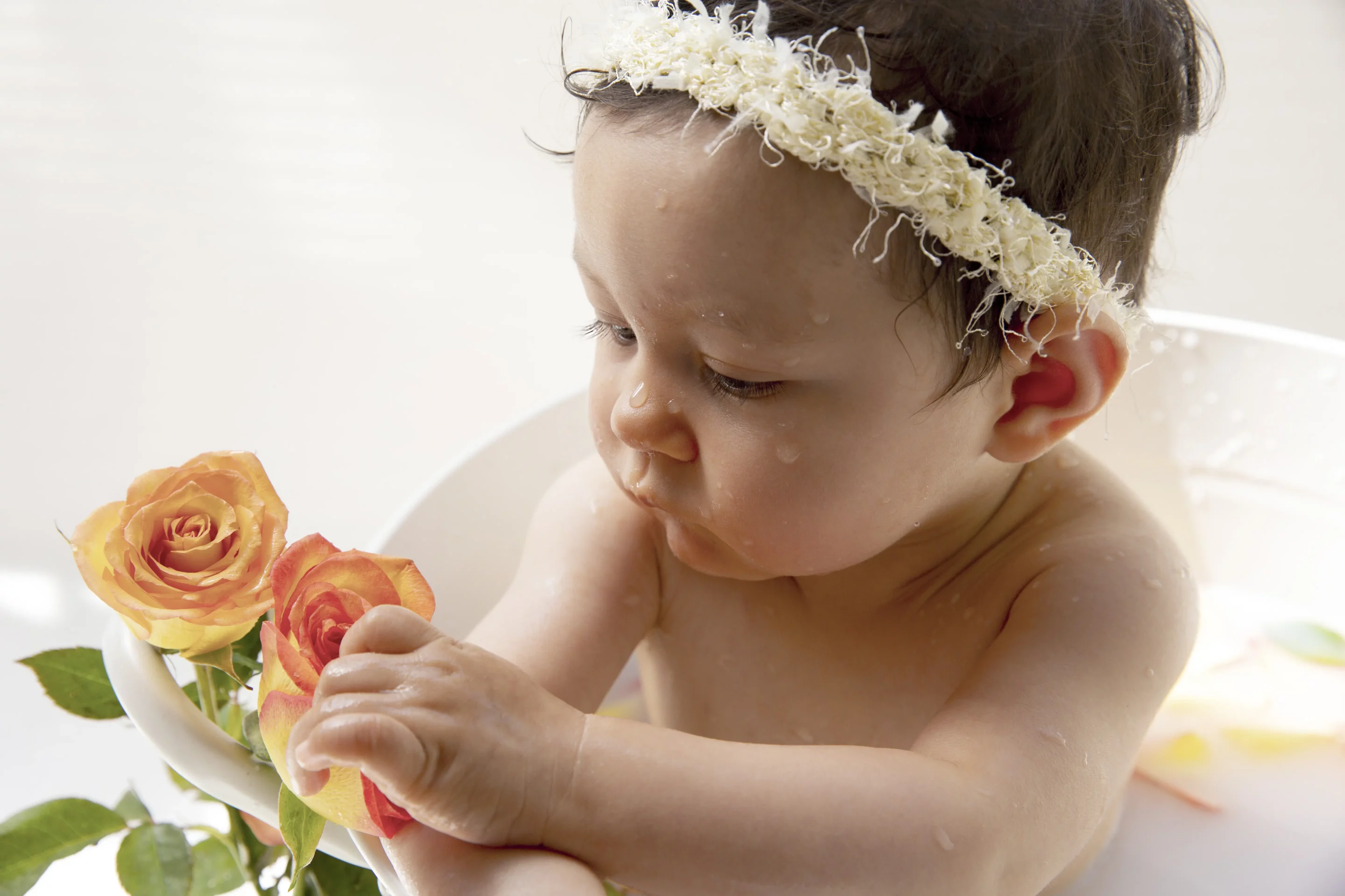 bain-de-lait-bébé-studio photo de bain de lait d'une petite fille qui découvre des roses oranges