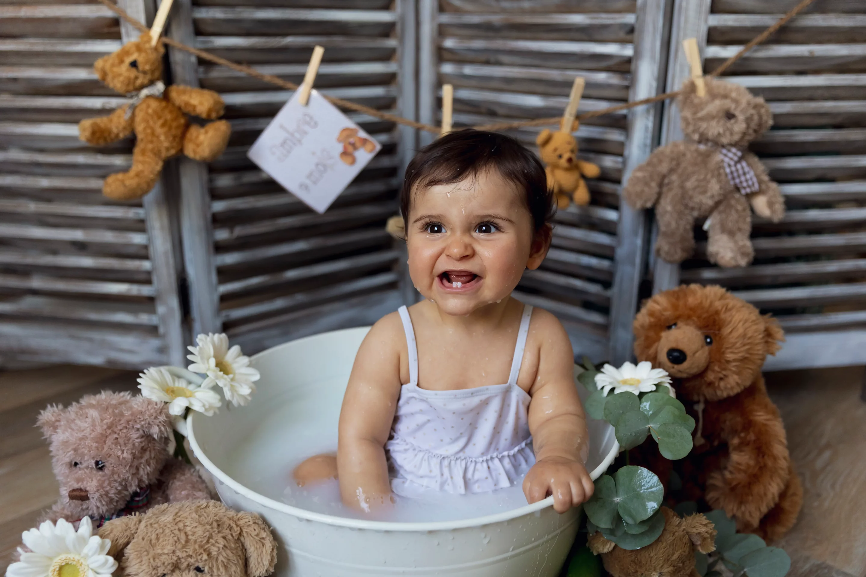 photo bain de lait d'une petite fille souriante, entourée de peluches et de fleurs