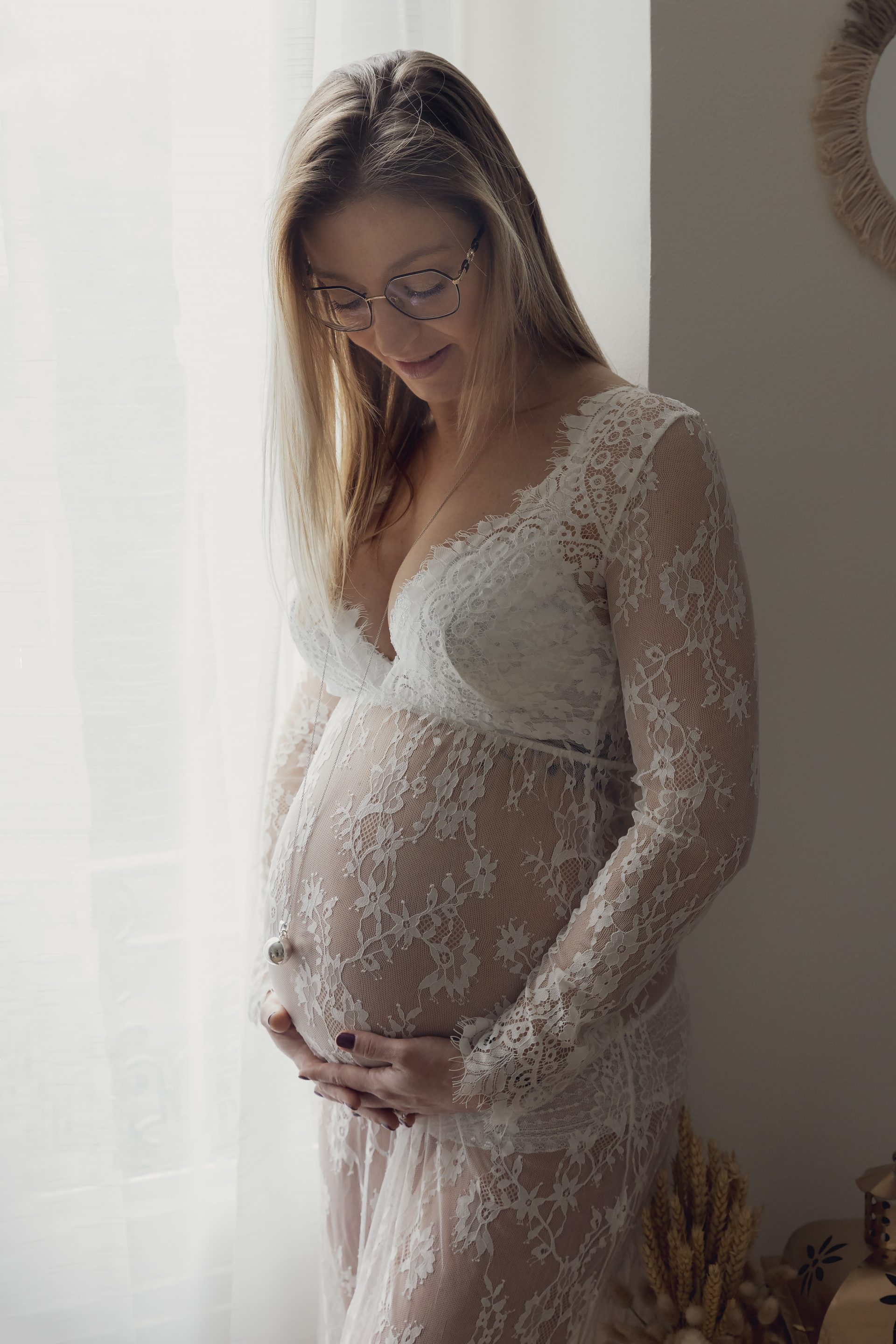 shooting-studio-grossesse-nice photo de grossesse d'une maman regardant son ventre, habillée d'une robe en dentelle blanche