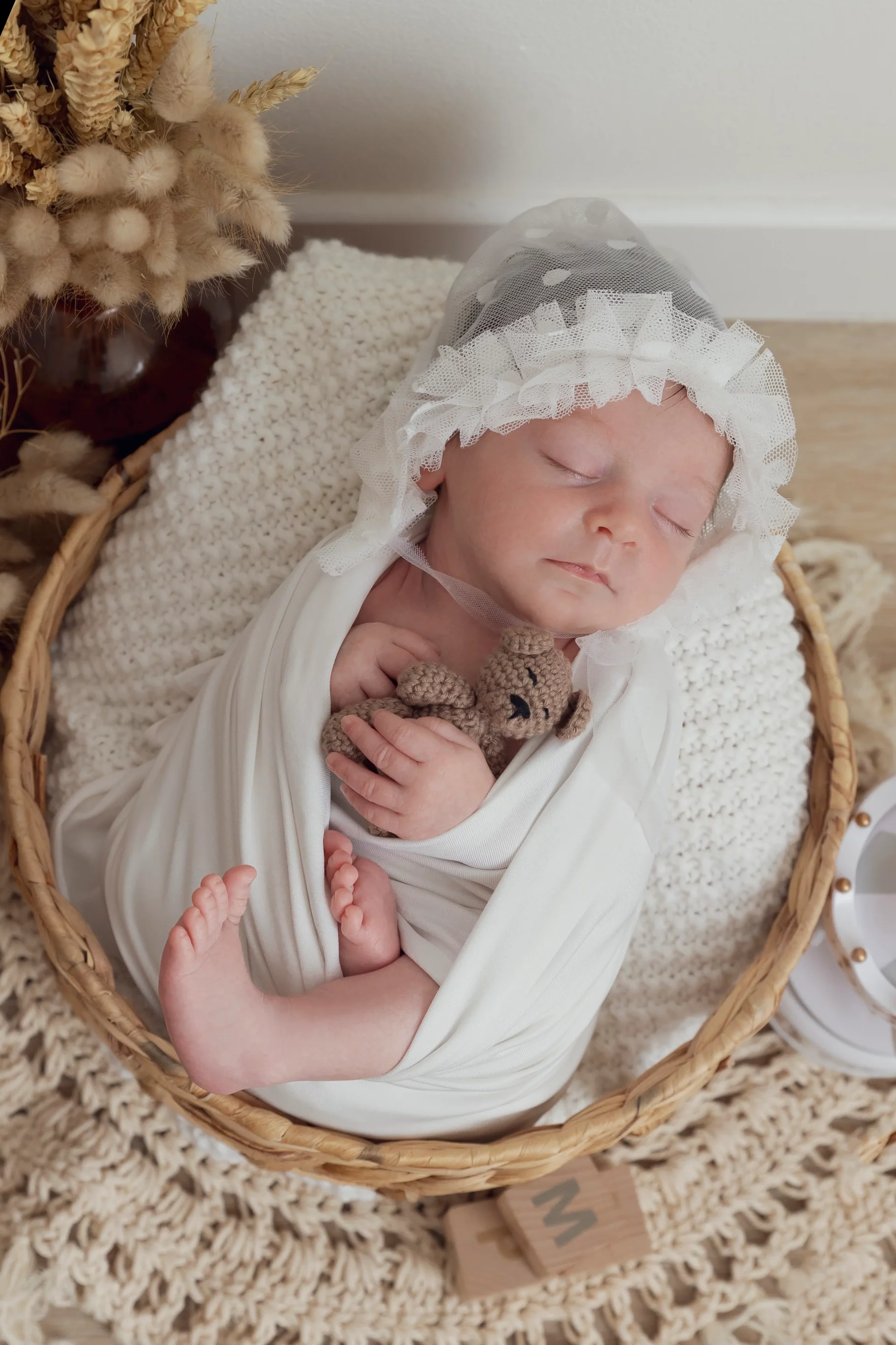 photo de naissance d'un bébé emmailloté, dans un panier, tenant un ourson dans ses mains