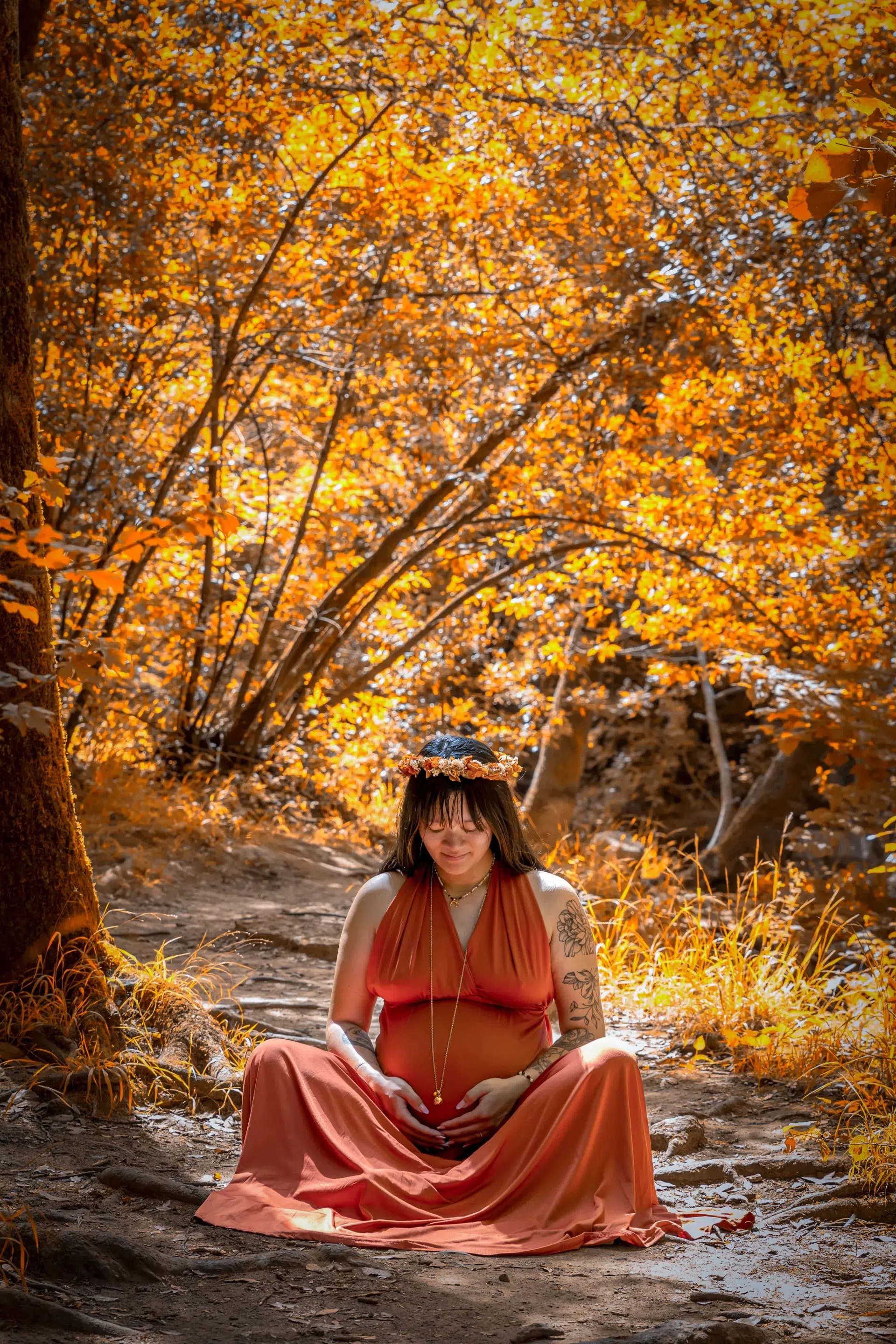 photo-grossesse-automnale photo de grossesse d'une femme assise en tailleur dans une forêt automnale