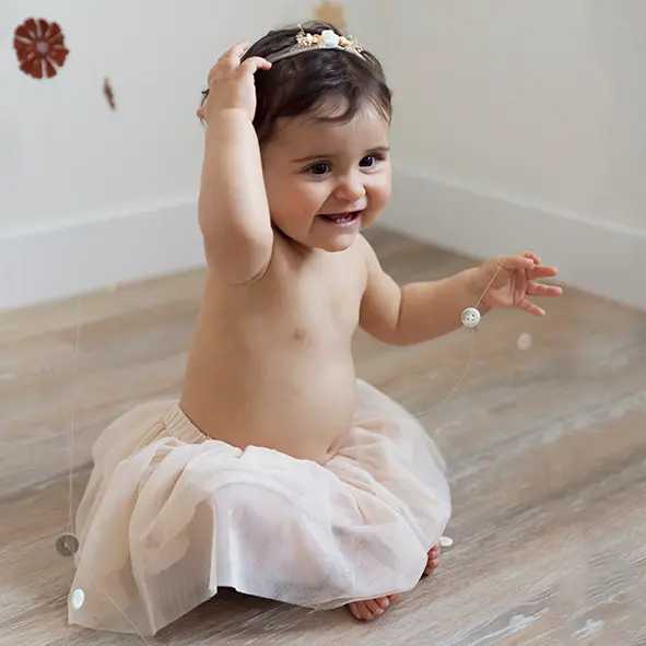 photo d'une petite fille de 9 mois souriante et habillée d'un tutu rose, assise dans un studio photo à nice sandra-alvoet-photographe