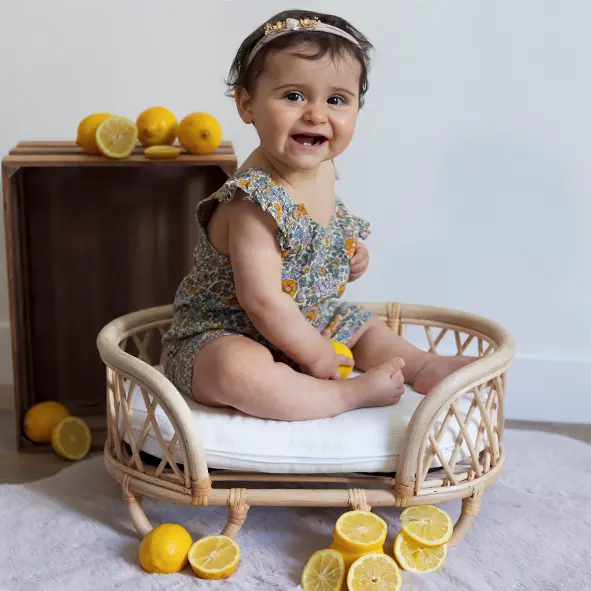 petite fille de 9 mois assise dans un petit lit en rotin dans un studio photo entourée de citrons sandra-alvoet-photographe
