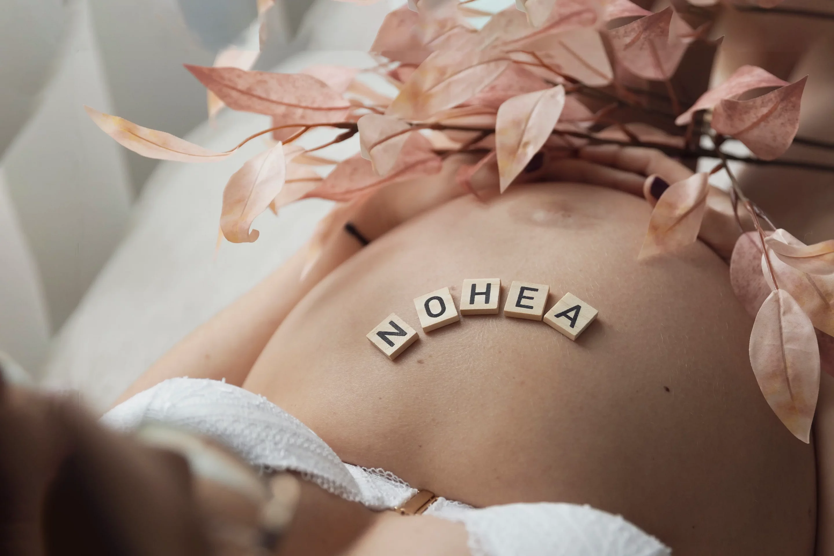 studio-nice-maternite-photo photographie ne gros plan d'un ventre de future maman avec le prénom du bébé écrit sur son ventre et des fleurs roses sandra-alvoet-photographe