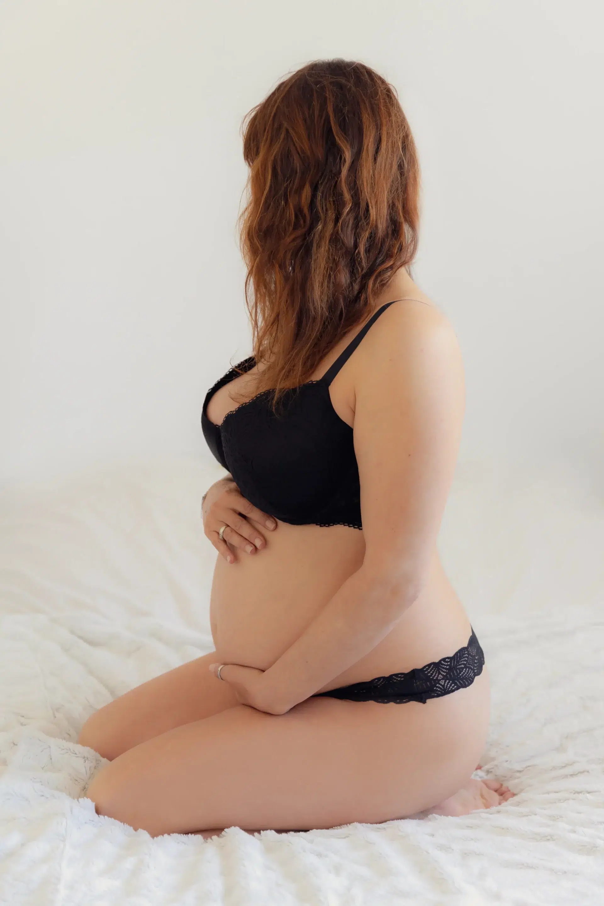 femme-enceinte-nice photographie d'une future maman agenouillée sur une couverture, tenant son ventre et tournant la tête sandra-alvoet-photographe