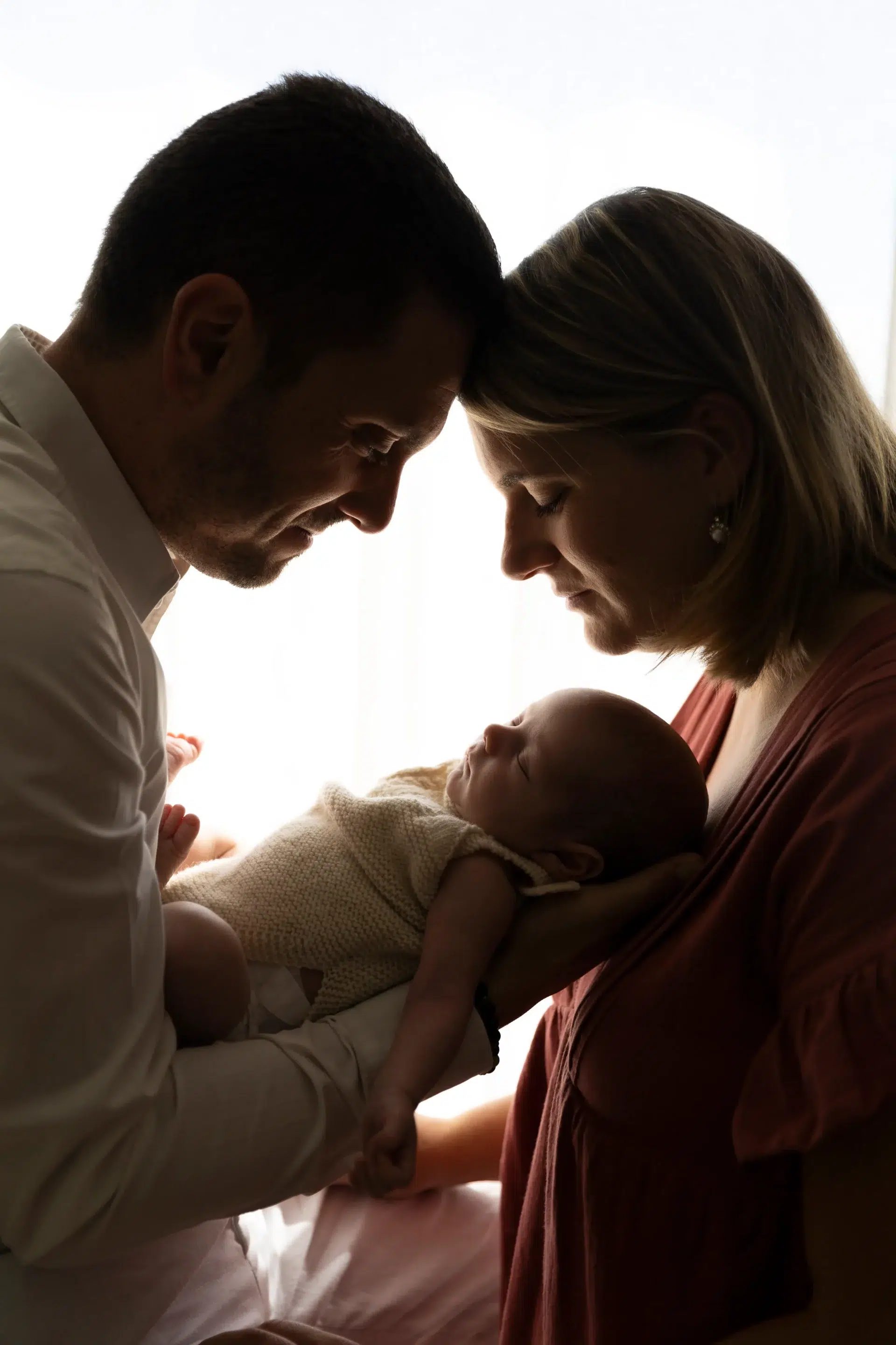 photo de naissance en contre jour de deux parents front contre front, regardant leur nouveau né