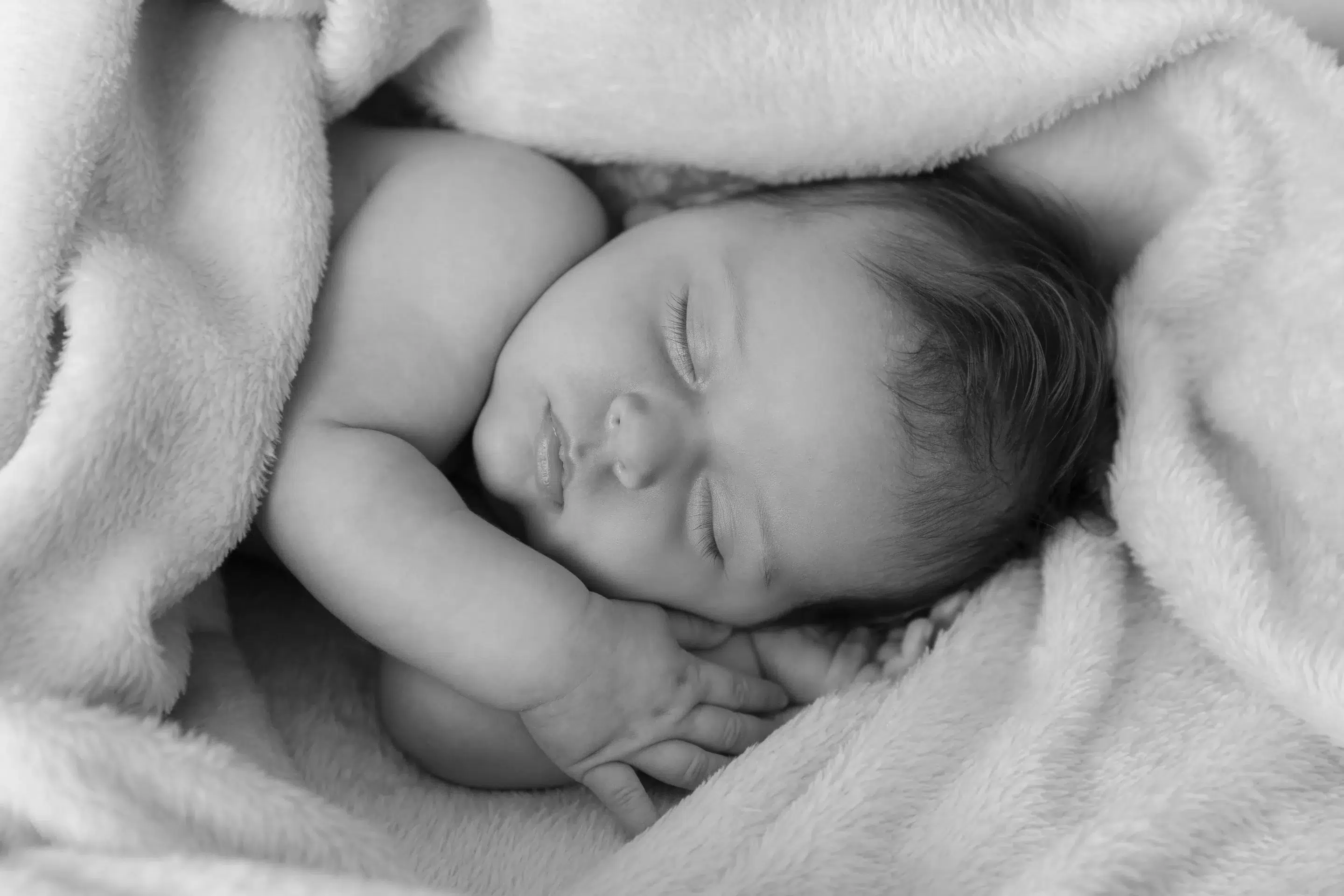 photographie de naissanceen noir et blanc d'un bébé endormi, ses deux mains posées sous sa tête