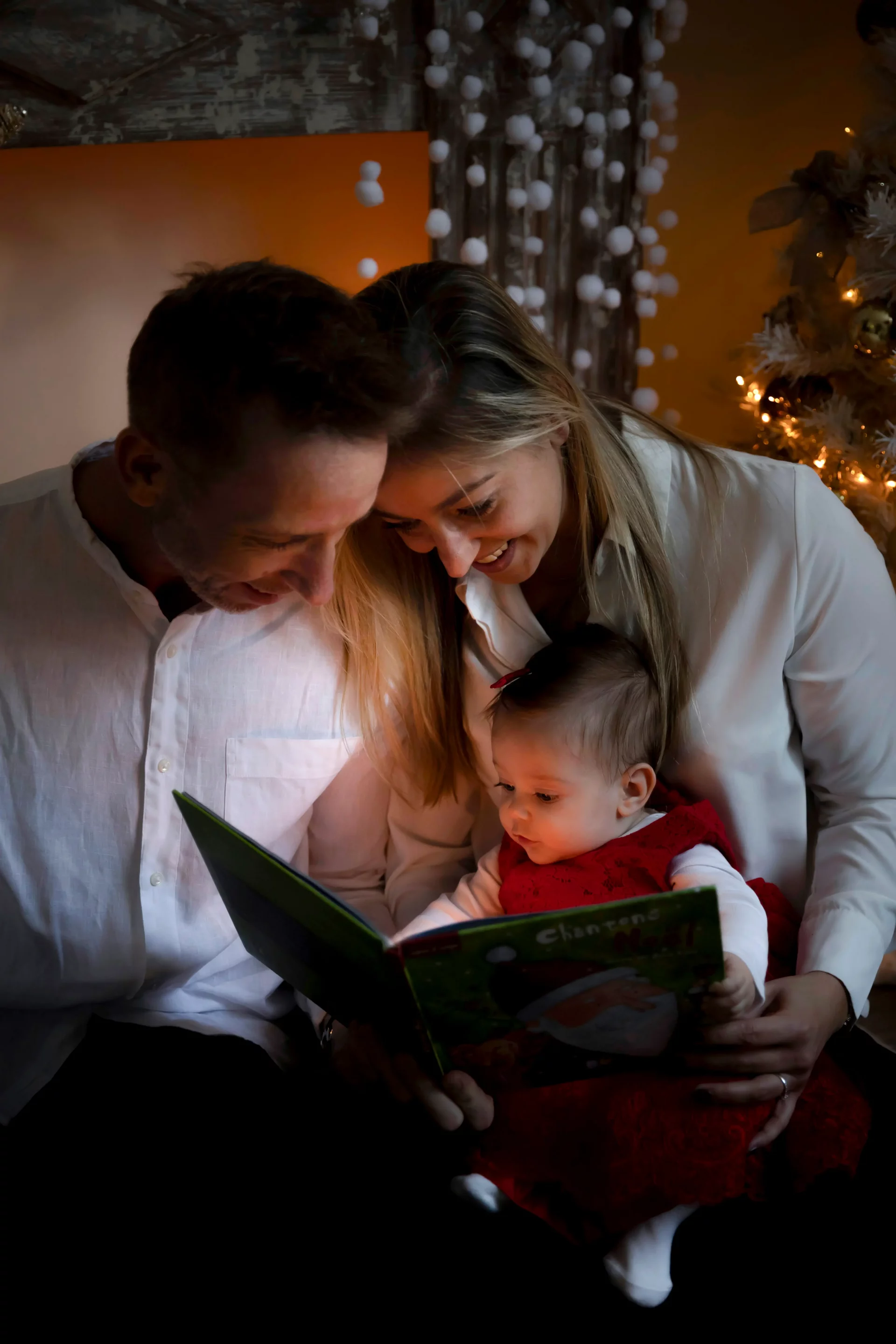 photo-famille-nice-noel photo de famille d'un couple qui lit un livre à son bébé, avec une lumière spéciale de Noël