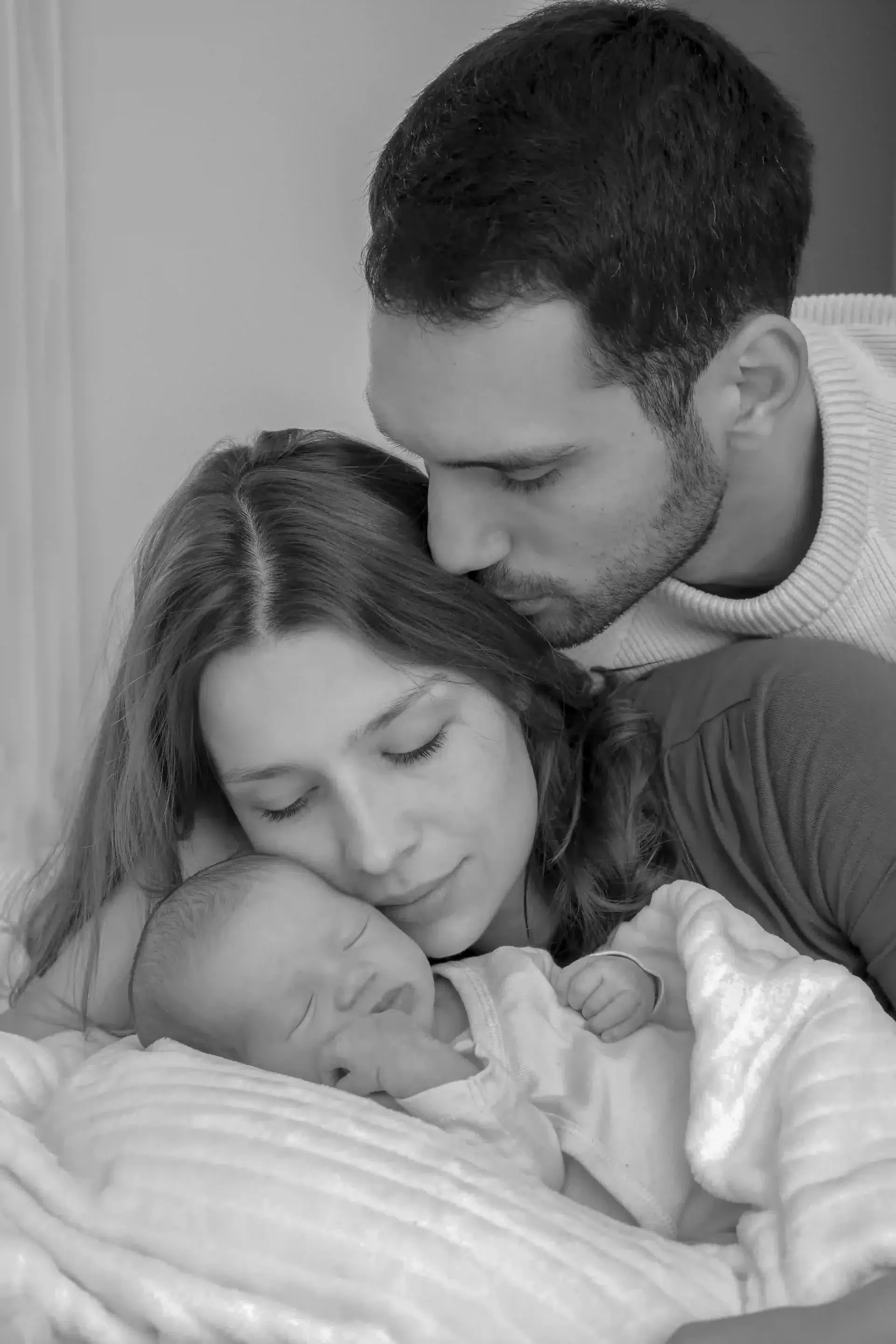 photo de naissance d'un père qui embrasse sa femme à côté de son bébé
