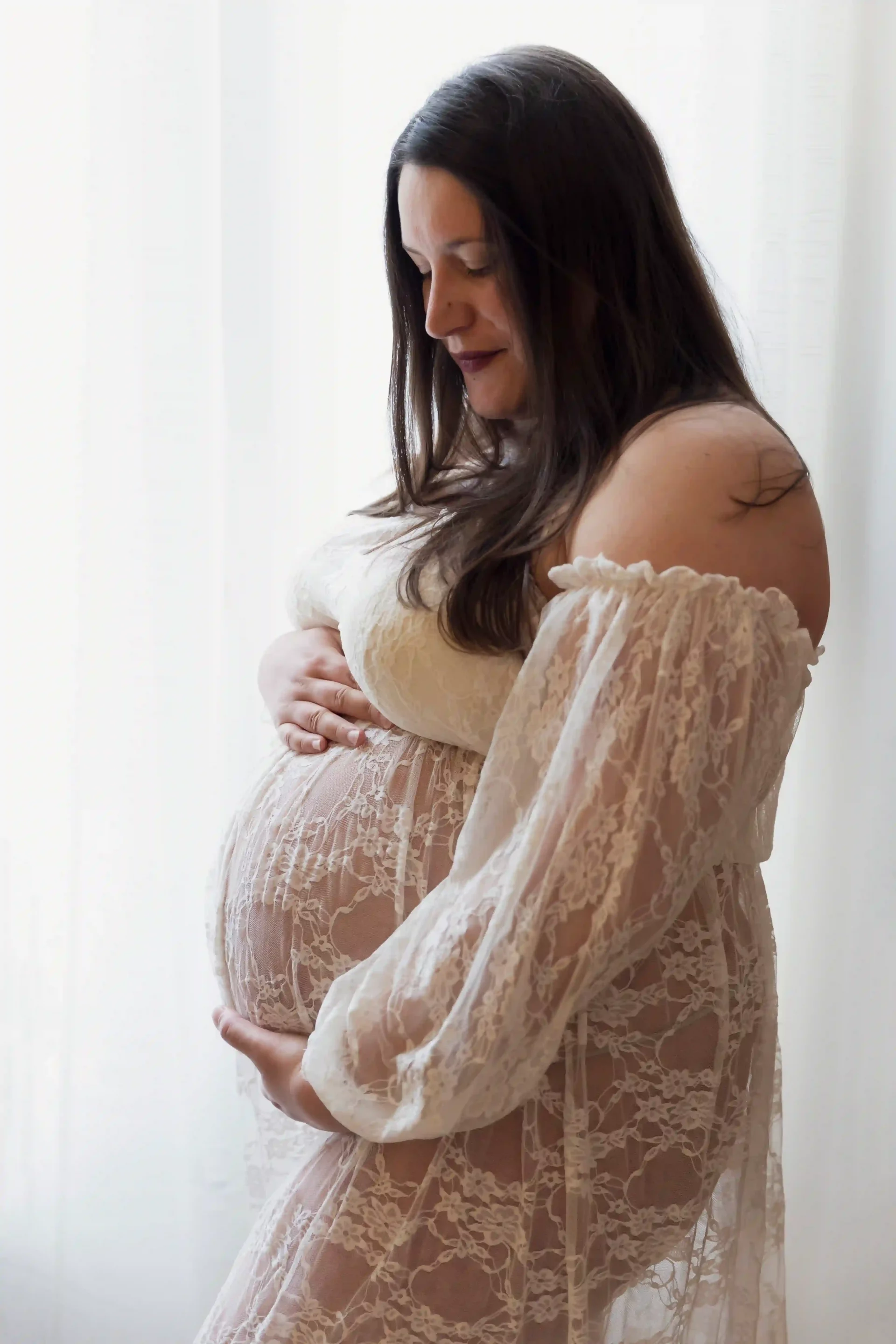 photo de grossesse d'une maman habillée en robe de dentelle blanche et regardant son ventre