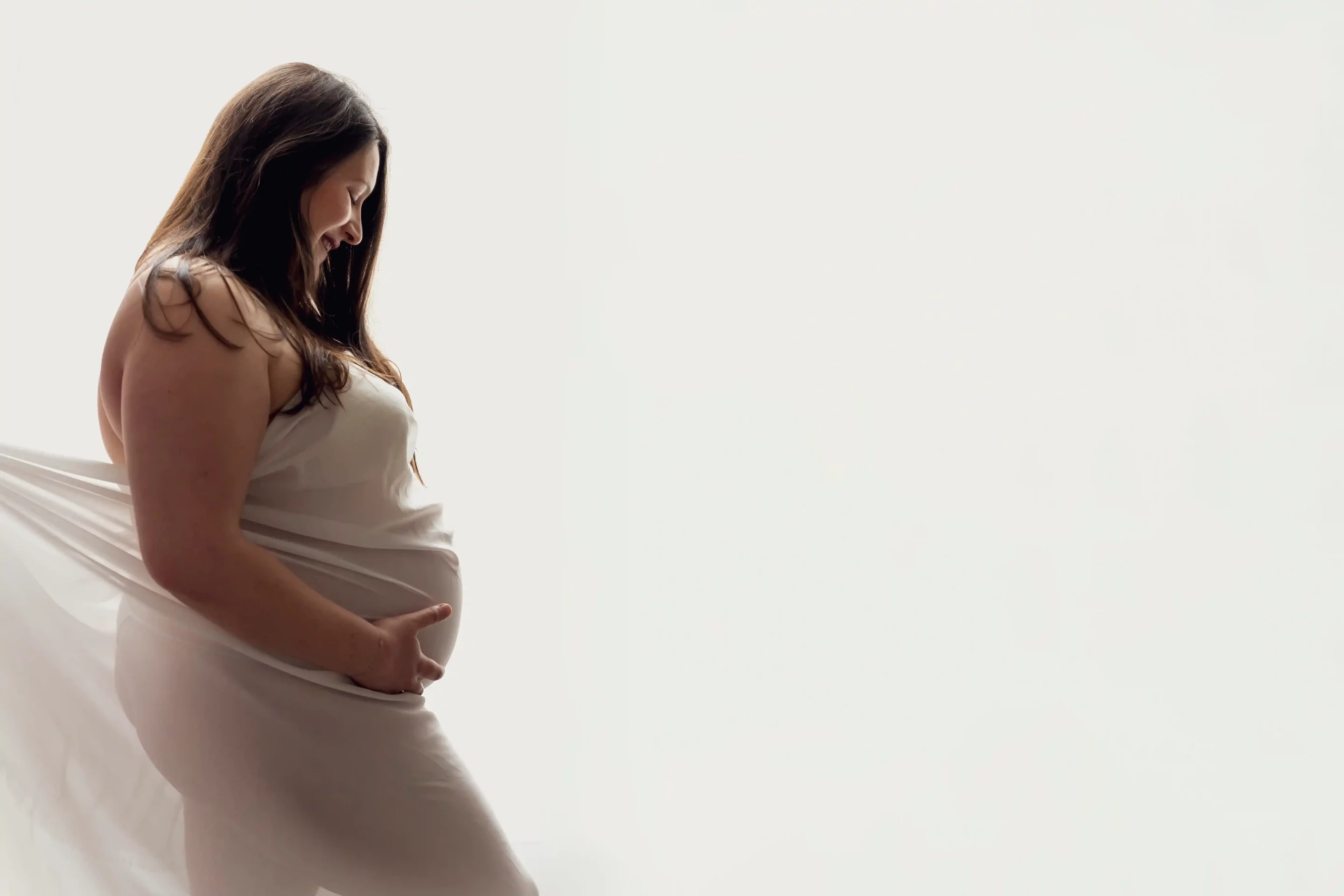 photo de grossesse, d'une femme habillée d'un drapé blanc, regarde son ventre