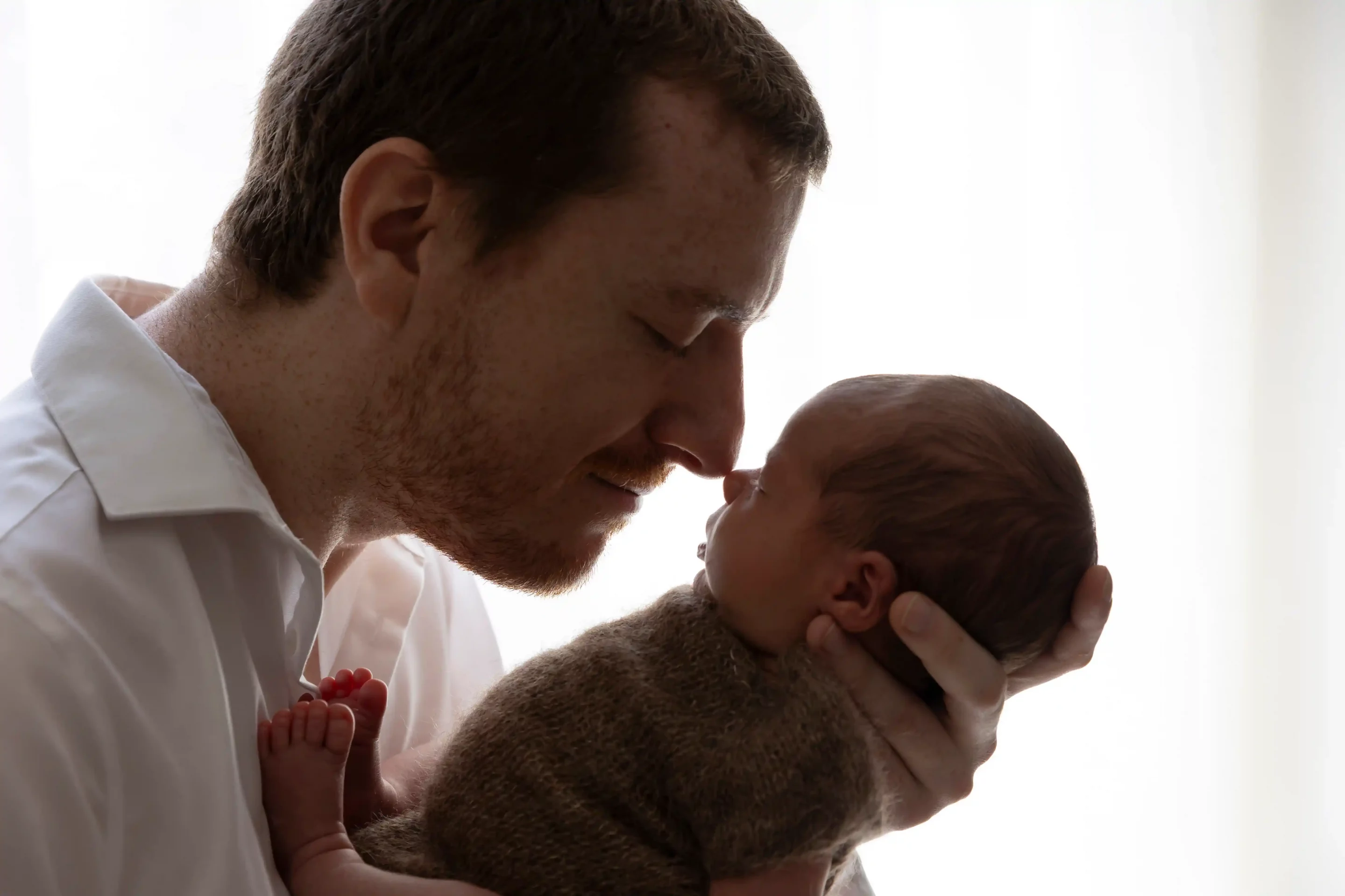 photo de naissance, un papa fait un bisou esquimau à son bébé. photo en ombre et lumière