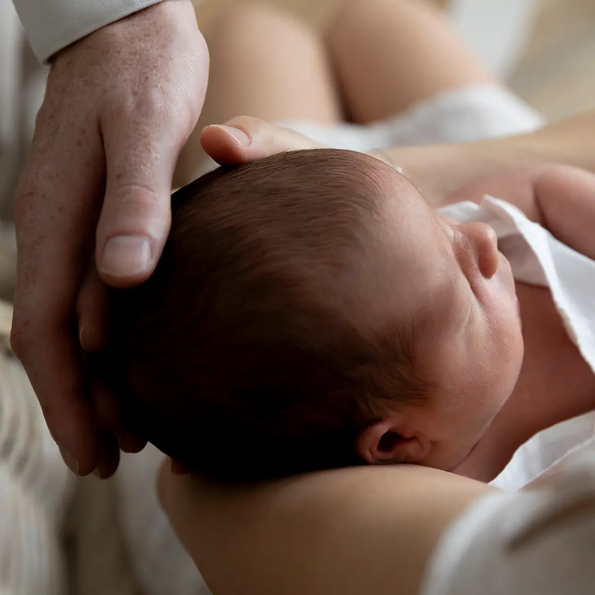 photo de naissance, gros plan sur la tête du bébé avec la main du papa posée dessus