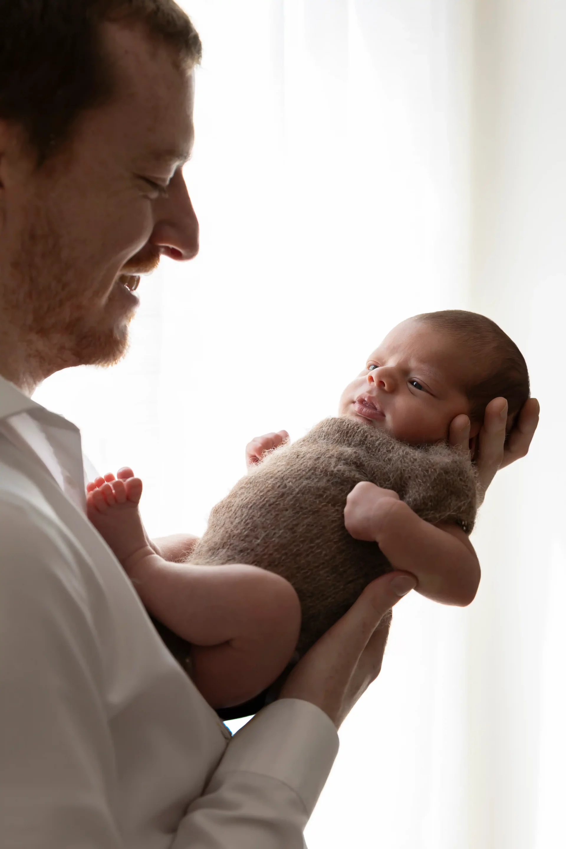 photo de naissance, d'un papa qui admire son bébé en le portant devant lui