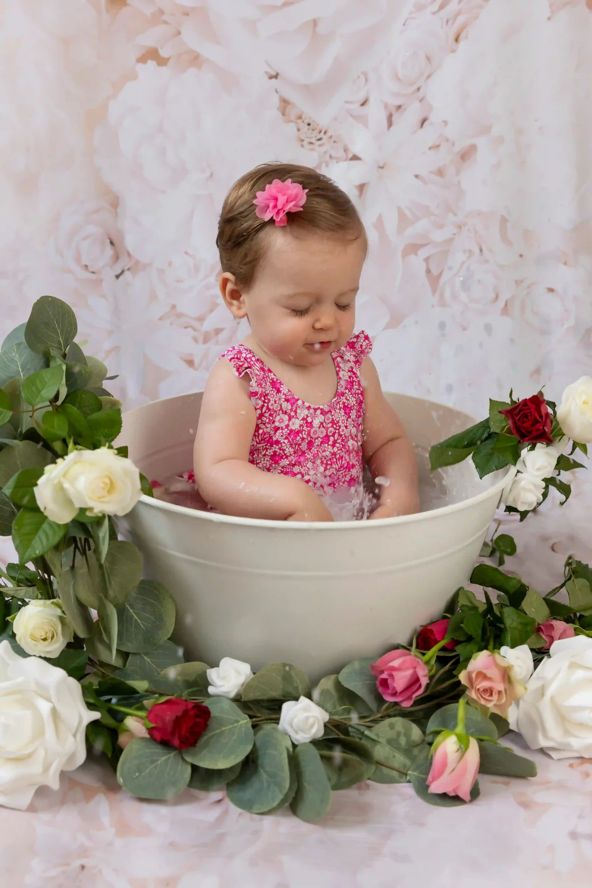 photo de bain de lait, d'une petite fille éclaboussant l'eau du bain, entourée de roses roses