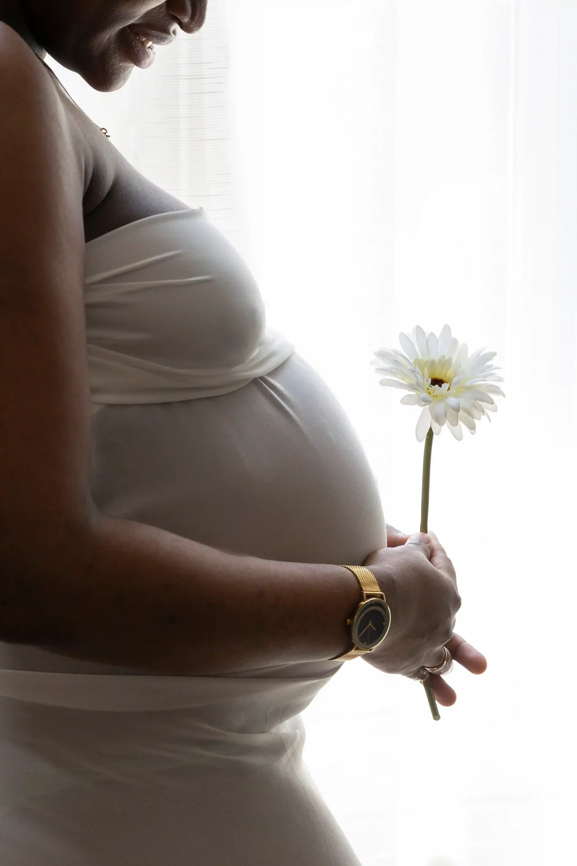 photo de grossesse, d'une maman qui tient une fleur blanche devant son ventre