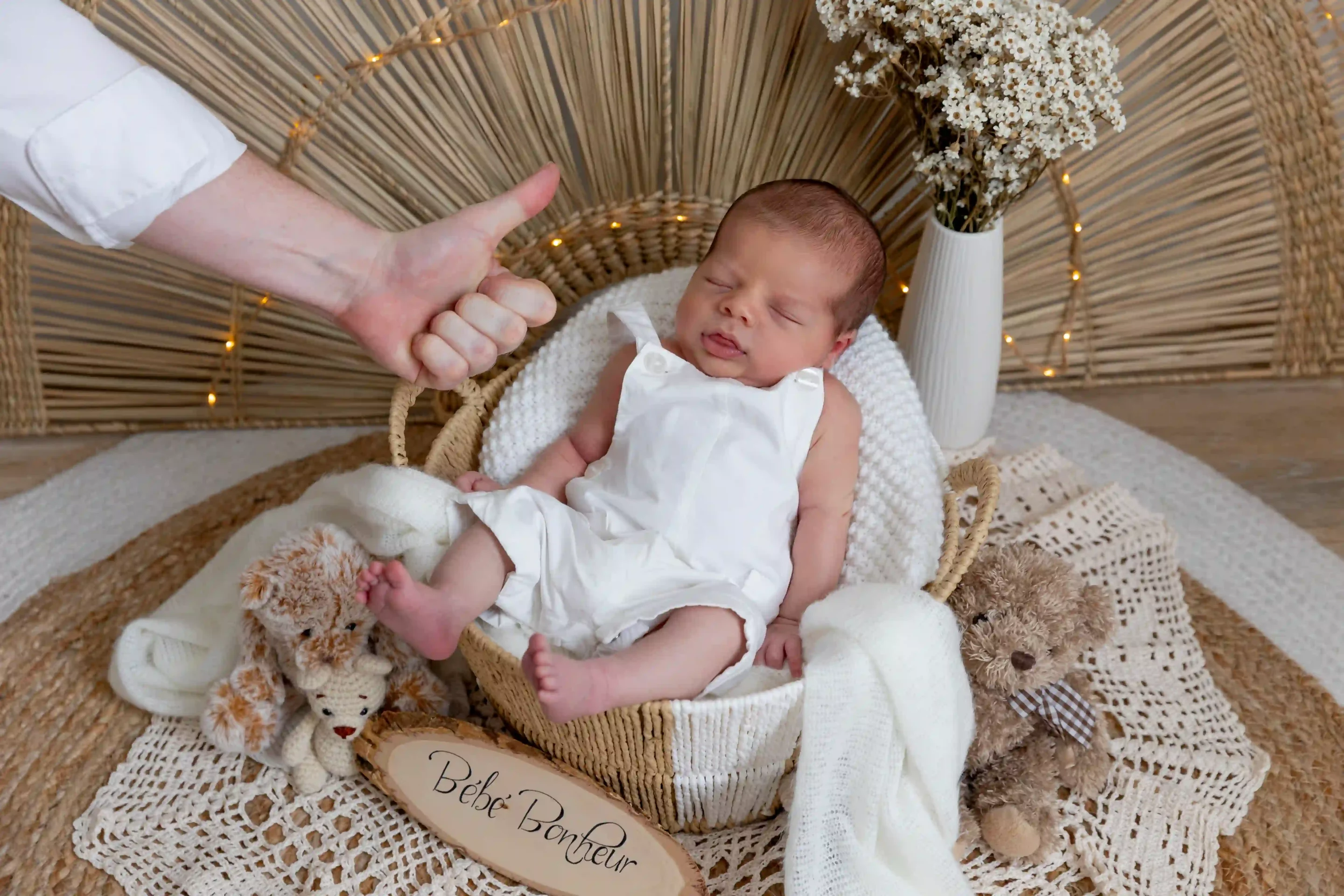 photo de naissance, d'un bébé endormi dans un panier et surplombé du pouce en l'air du papa