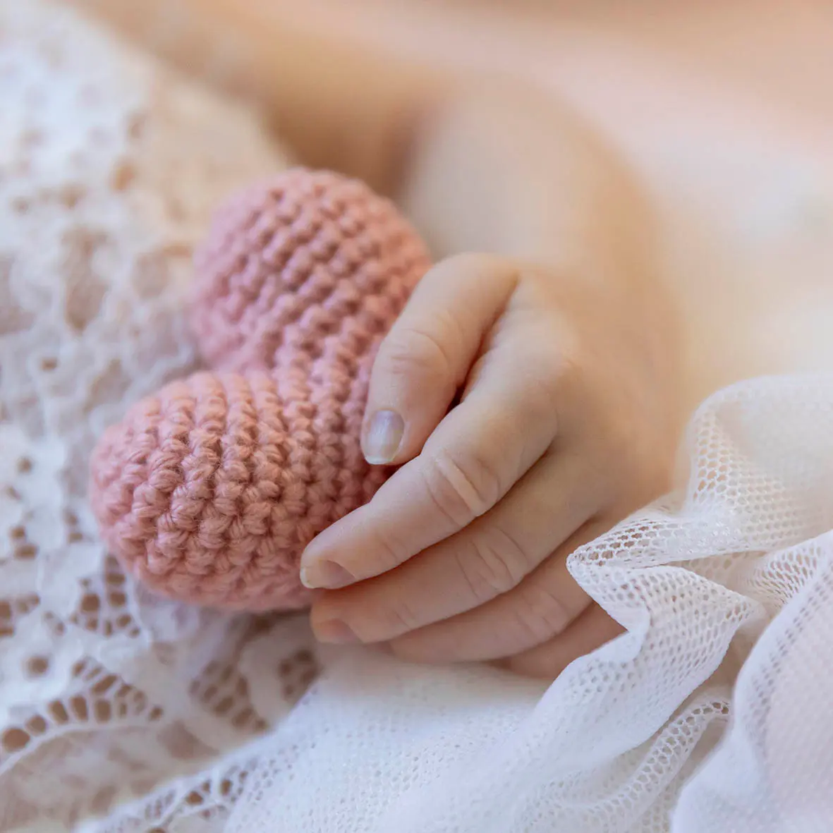 photo de naissance, d'une petite main de bébé tenant un cœur rose encrochet