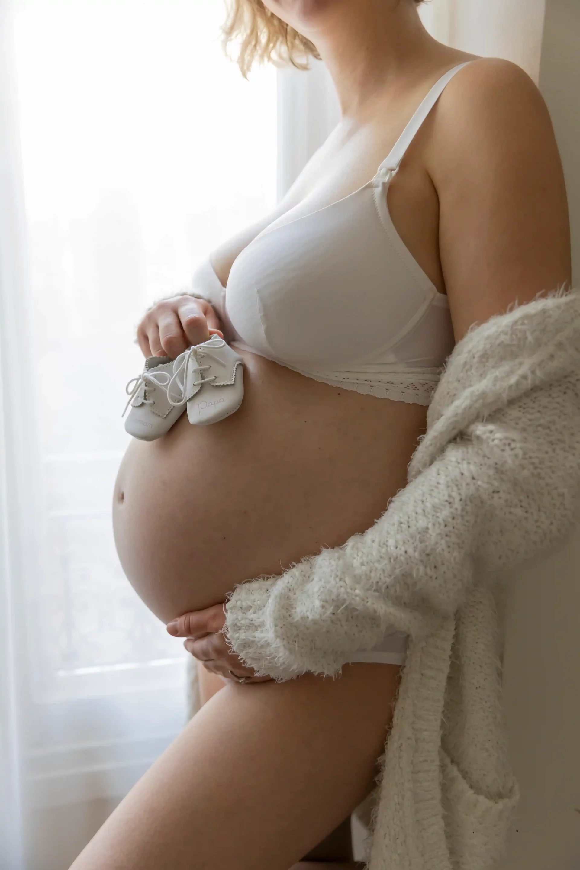 photo de grossesse, gros plan sur les petits chaussons posées sur le ventre de la maman