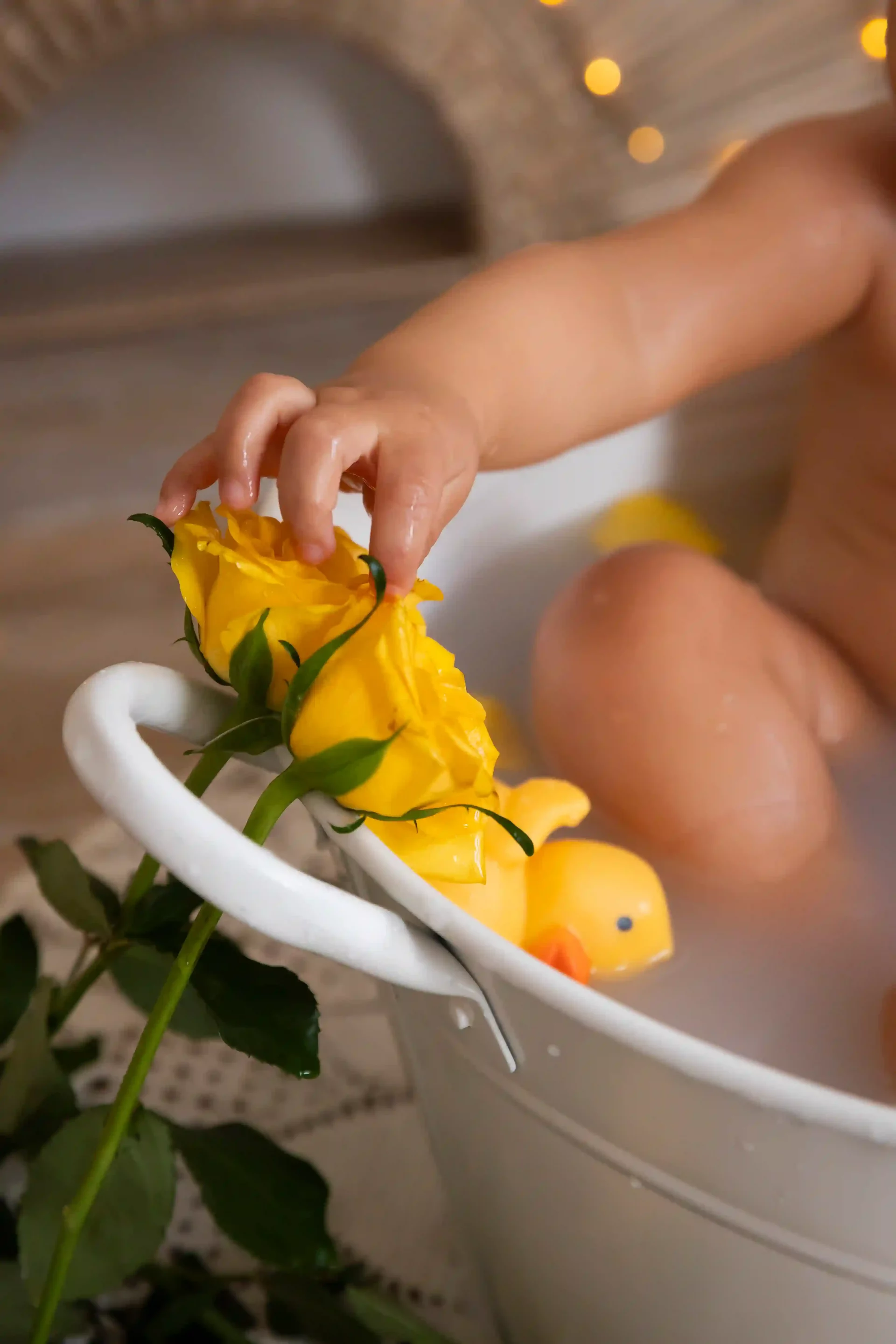 photo bain de lait, gros plan sur la main du bébé touchant une rose jaune