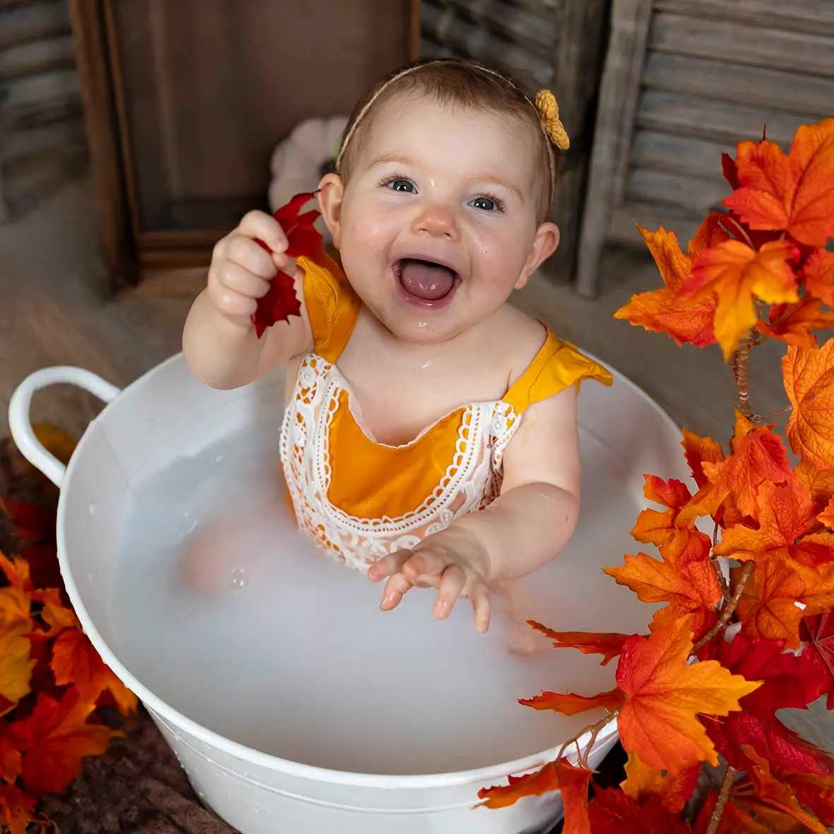 photo de bain de lait, petite fille rousse entourée de feuilles d'automne, qui sourit