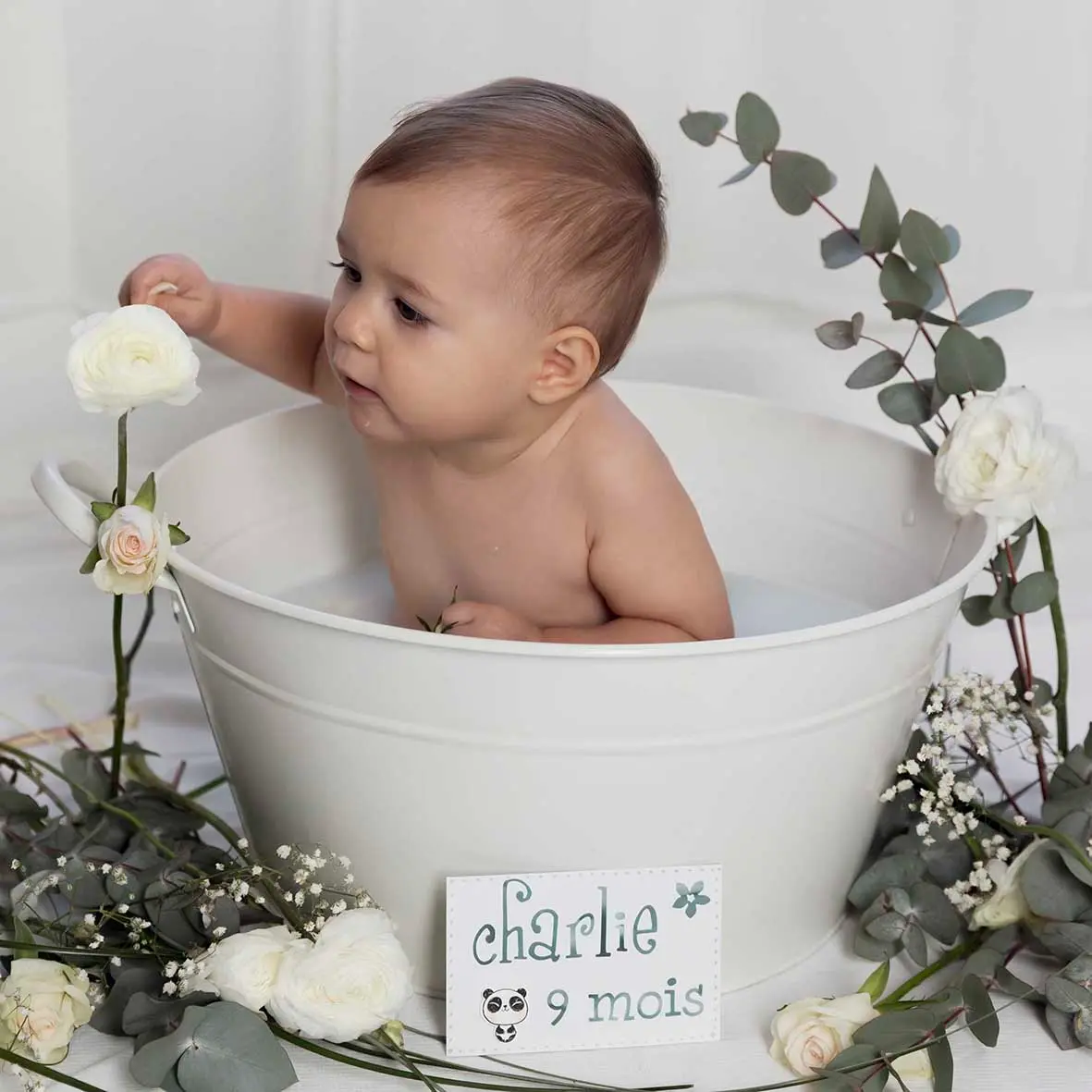 photo bain de lait, bébé dans une bassine, entouré de fleurs blanches