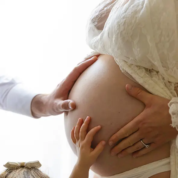 photo de grossesse, la main du papa, de la maman et de la grande sœur posées sur le ventre