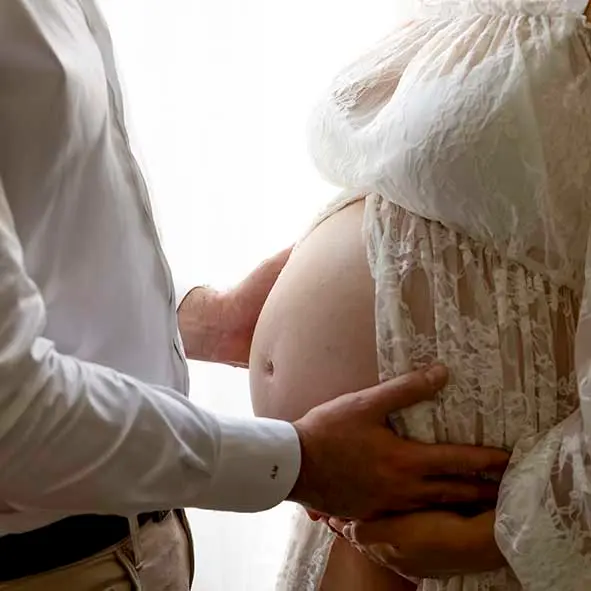 photo de grossesse, gros plan sur les deux mains du papa posées sur le ventre de la maman
