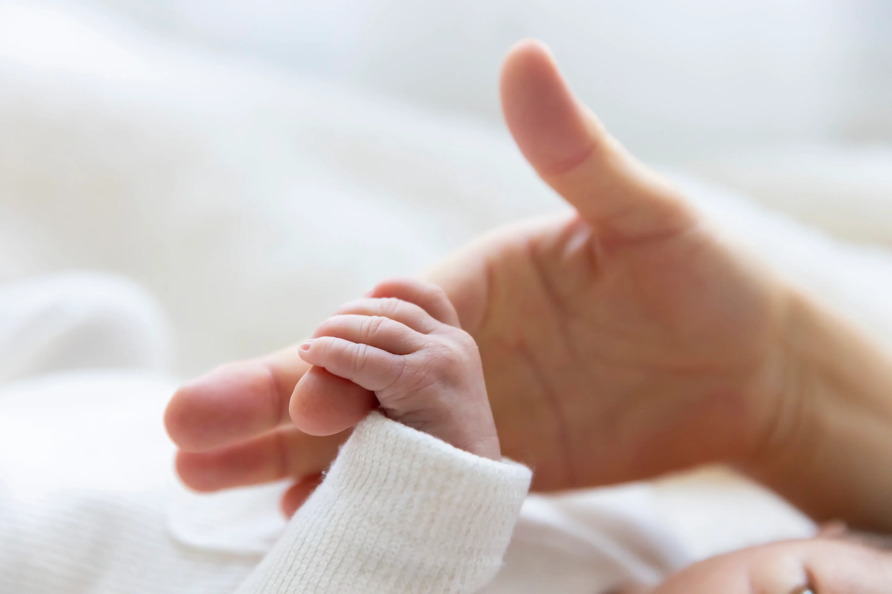 photo de naissance, gros plan sur la main du bébé qui tient celle de sa maman