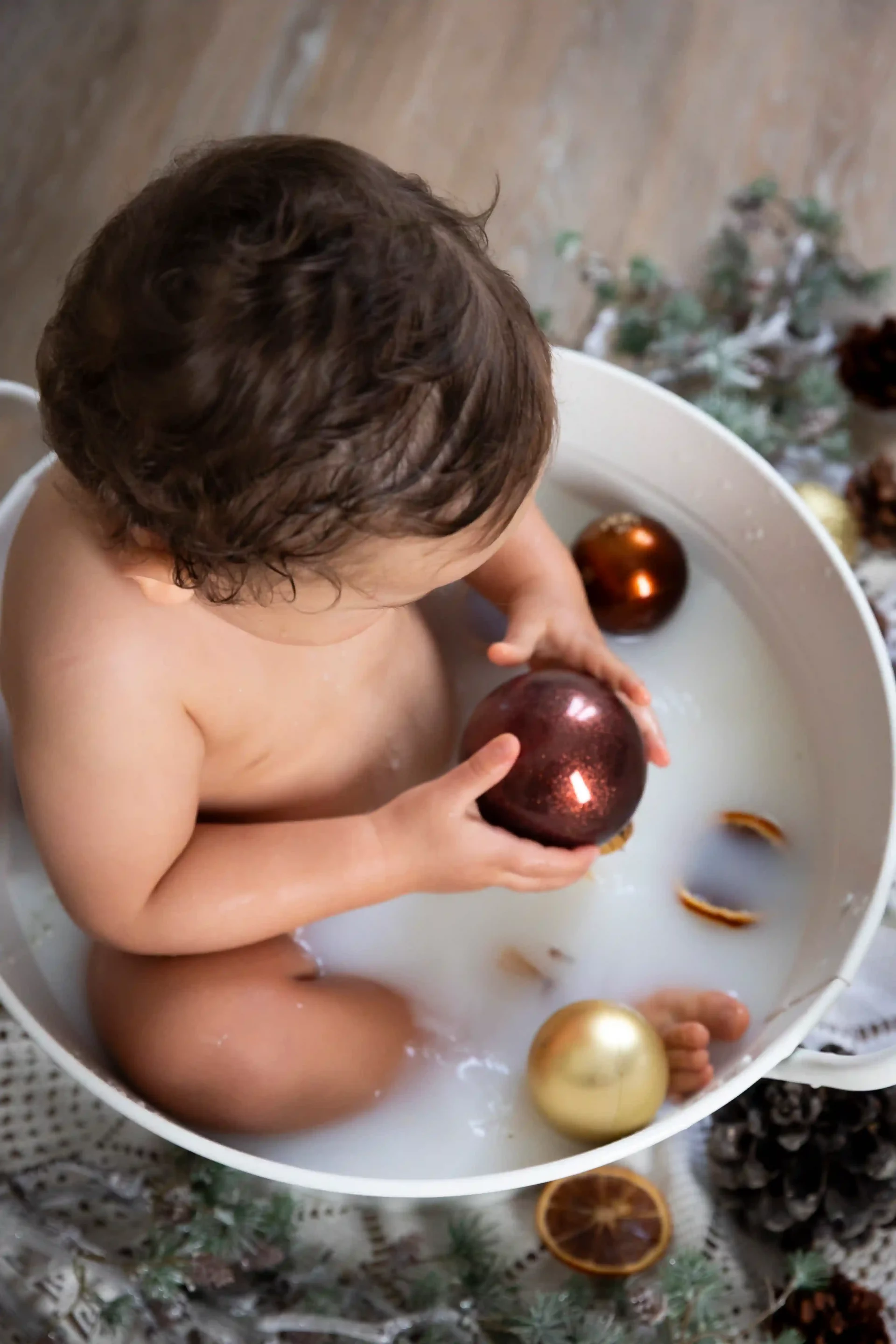 photo bain de lait version noël, un petit garçon tient une boule dans ses mains
