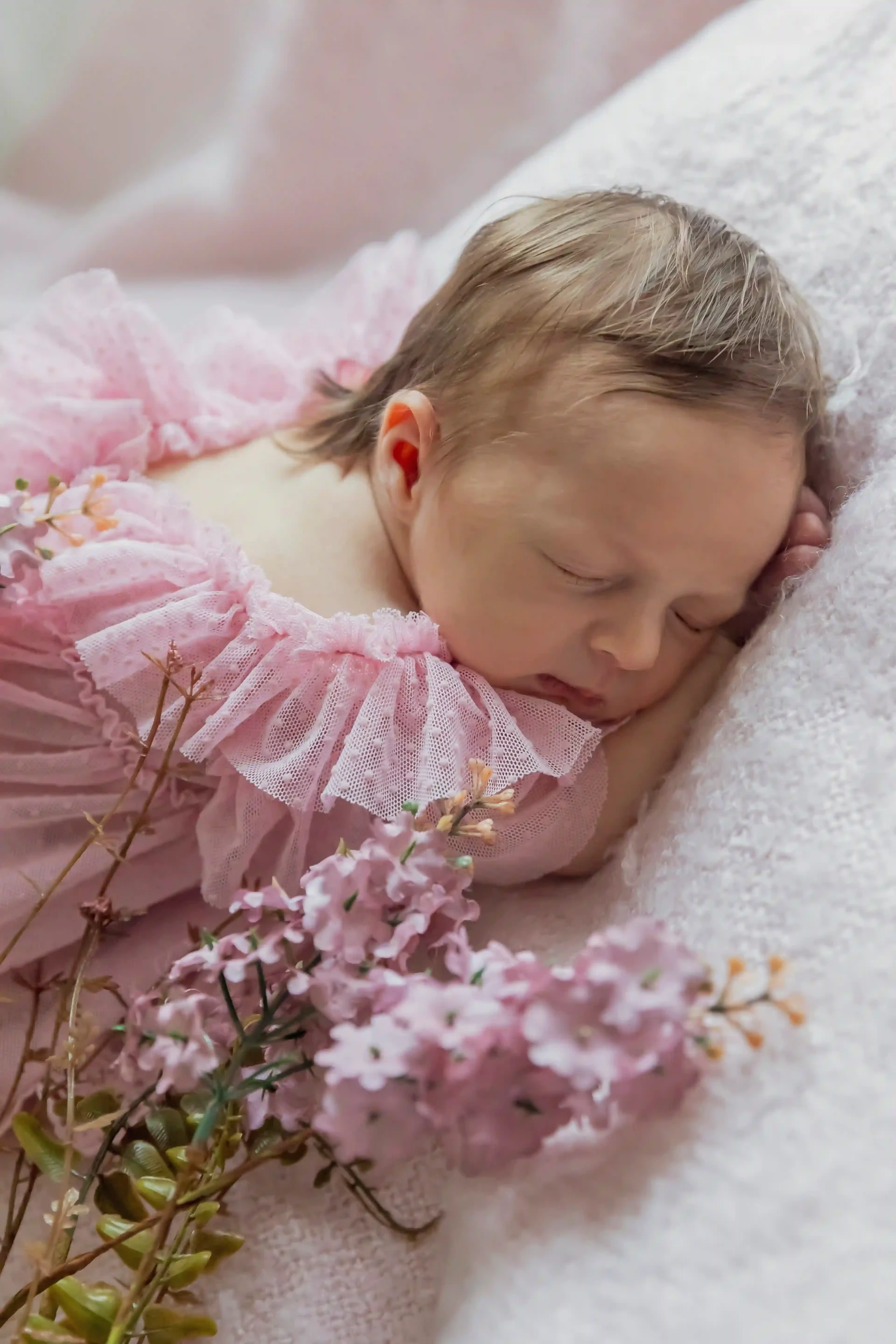 photo de bébé, endormie sur le ventre et entourée de fleurs roses