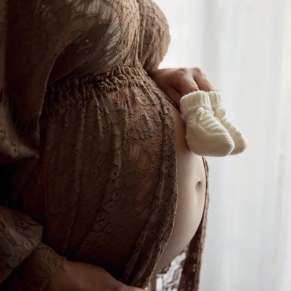 photo de grossesse, gros plan sur le ventre de la maman, vêtue d'une robe en dentelle marron