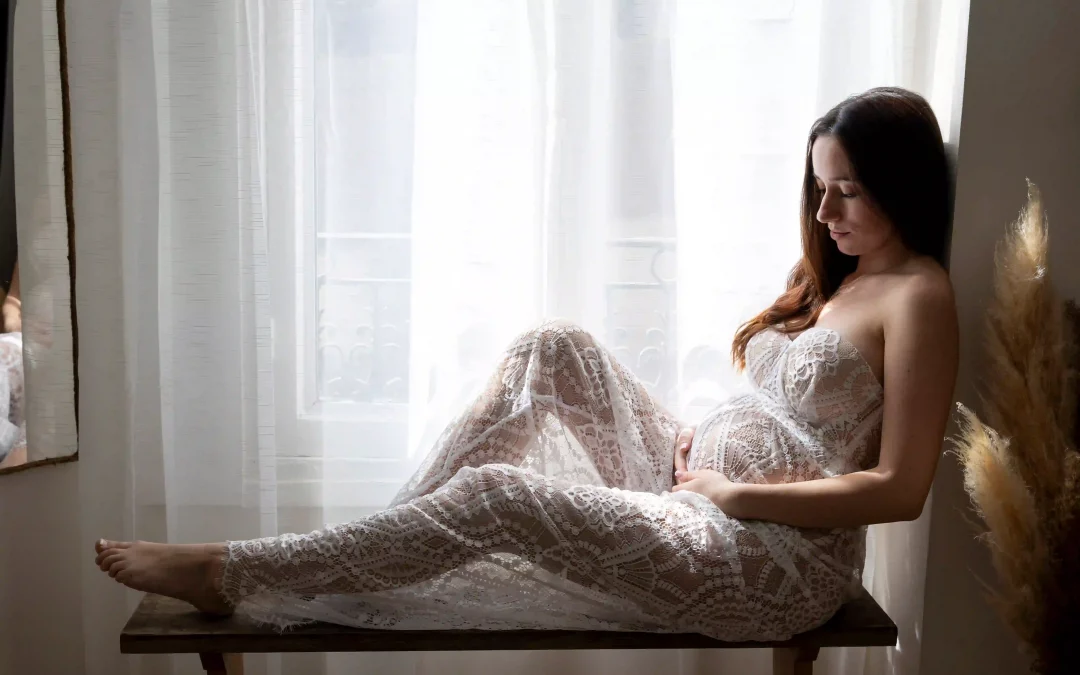 photo de grossesse, future maman assise sur un banc, en robe en dentelle blanche