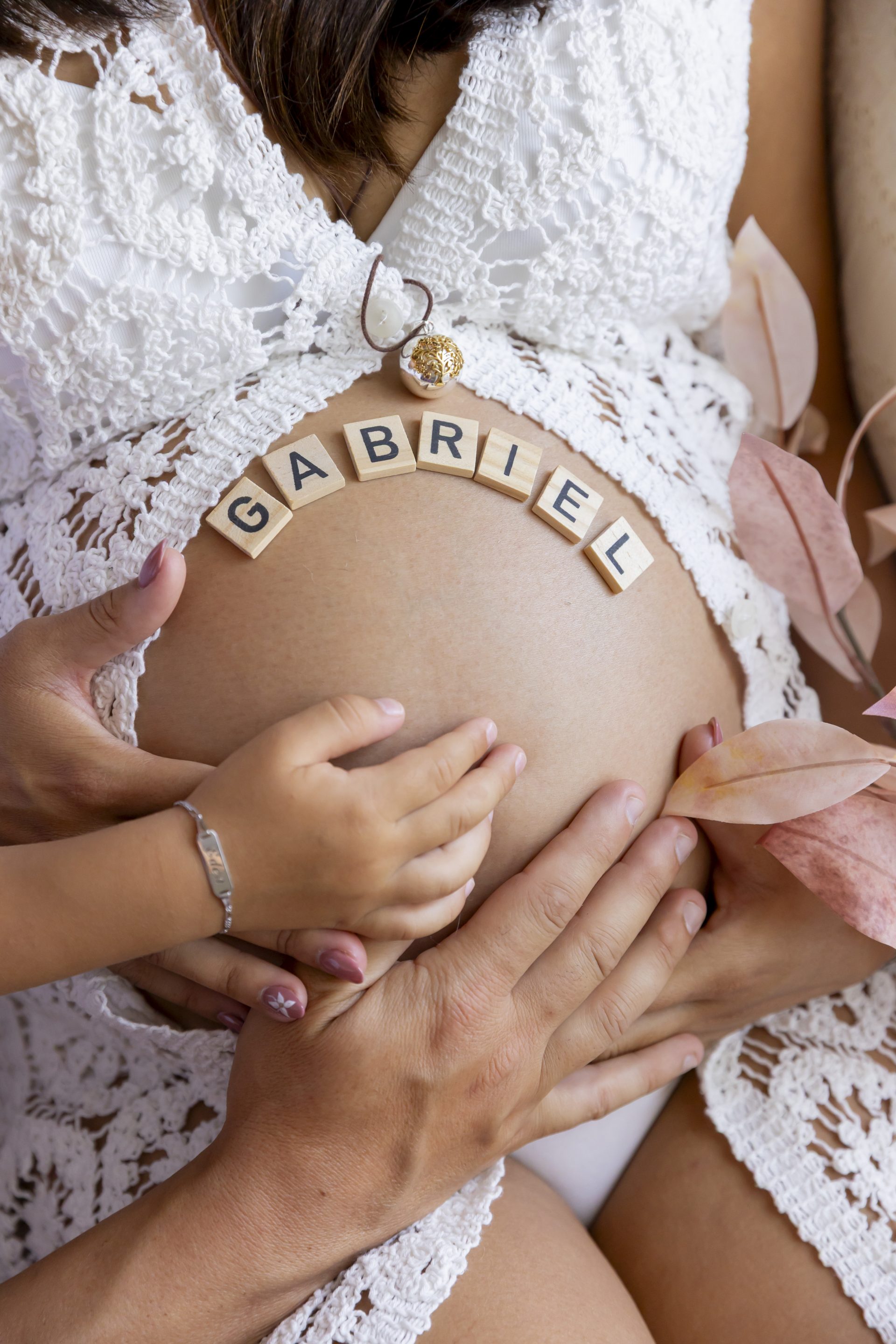 photo de grossesse, prénom du bébé écrit sur le ventre et les mains de toute la famille posées dessus